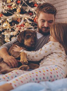 Dad and daughter cuddle dog with Christmas Tree in background